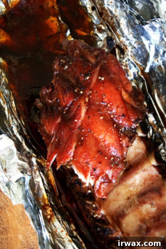 Αυτή η καταπληκτική συνταγή για baby back ribs χρειάζεται πέντε λεπτά προετοιμασίας, αλλά αυτό που βγαίνει από τον φούρνο – ένα ζουμερό πακέτο από baby back ribs που πέφτουν από το κόκαλο, τέλεια τραγανά εξωτερικά – έχει τη γεύση μιας ολόκληρης μέρας δουλειάς πάνω από μια ψησταριά γεμάτη κάρβουνα. Γλυκά. Καπνιστά. Αλμυρά. Νόστιμα. Αν αυτά δεν είναι τα καλύτερα παϊδάκια που έχετε ετοιμάσει ποτέ, είναι τουλάχιστον καταπληκτικά παϊδάκια. // alexandracooks.com Κοντινό πλάνο από πάνω σε baby back ribs σε αλουμινόχαρτο