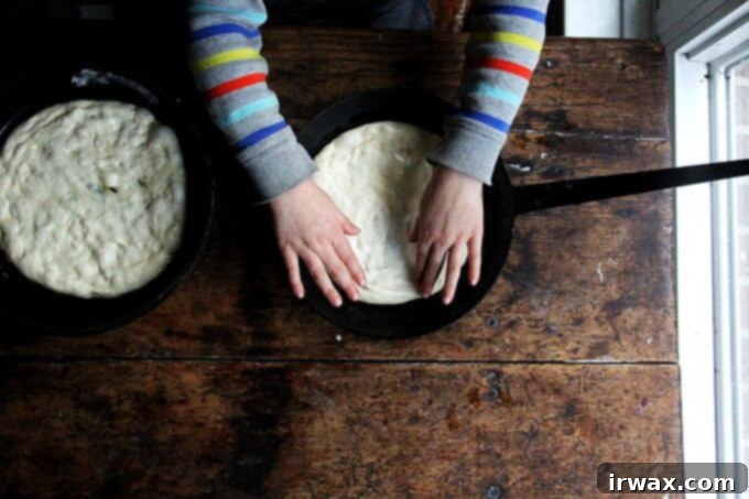 Making these skillet pizzas, I've come to realize, is a relatively good activity for involving children. For one, the dough doesn’t contain too many ingredients, and it’s forgiving—if flour spills out of the bowl, it’s easy to add more. More to the point, there are no eggs! Also, the many and varied steps of pizza making—mixing the dough, shredding the cheese, stretching and saucing the dough, topping the rounds—keeps the kids engaged. // alexandracooks.com Ένα παιδί απλώνει ζύμη πίτσας σε ένα τηγάνι.